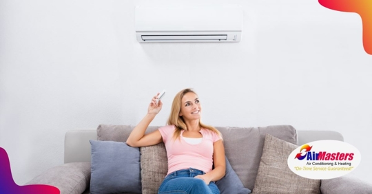 A woman smiling sitting on a couch pointing a remote at a ductless mini split ac mounted on the wall